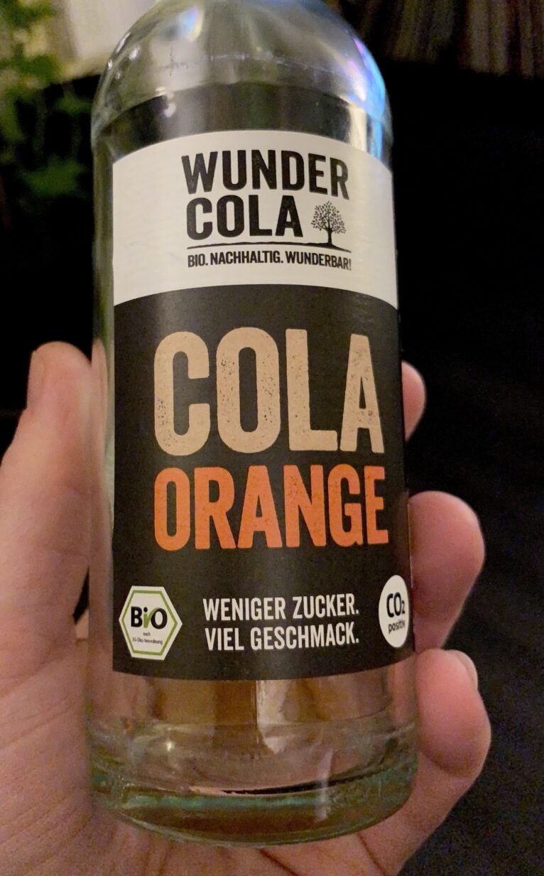 Hand hält eine Flasche „Wundercola – Cola-Orange“ in der Hand,